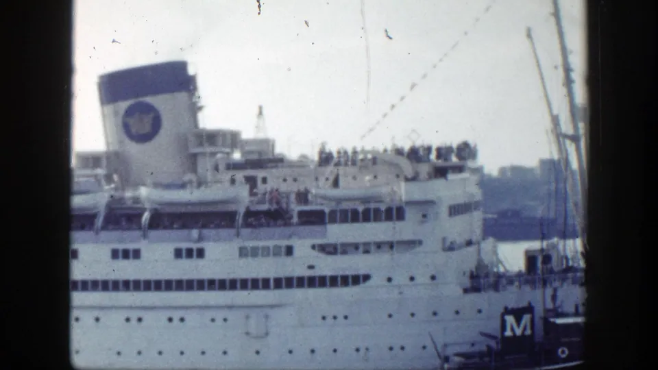 A docked ocean liner in New York, 1948, with passengers lining the upper deck and a blue funnel bearing a circular logo.