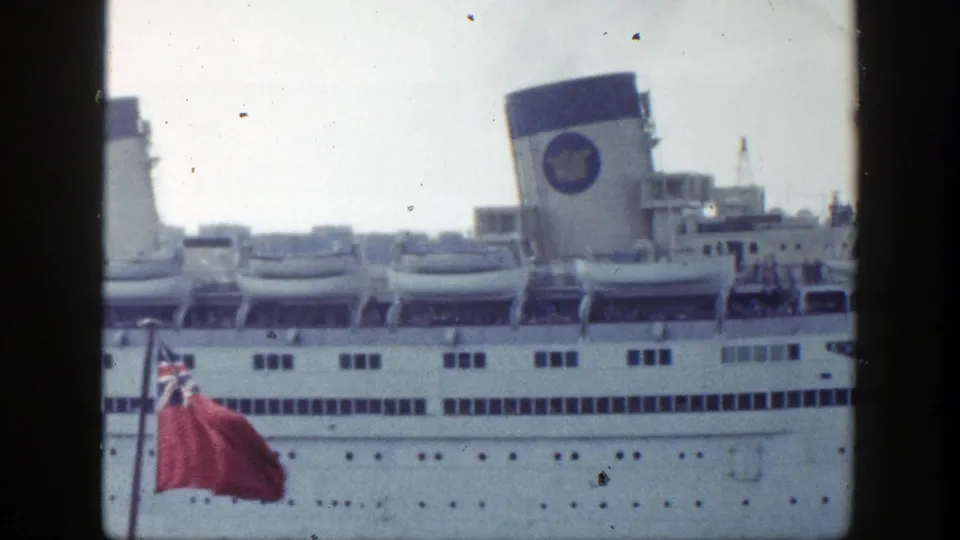 New York 1948 home-movie frame showing the liner broadside, with a red Union Jack-style flag moving in front of the hull.