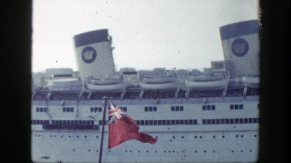 1948 New York harbor footage frame with a white passenger liner, twin logoed funnels, deck lifeboats, and a red Union Jack-style flag.