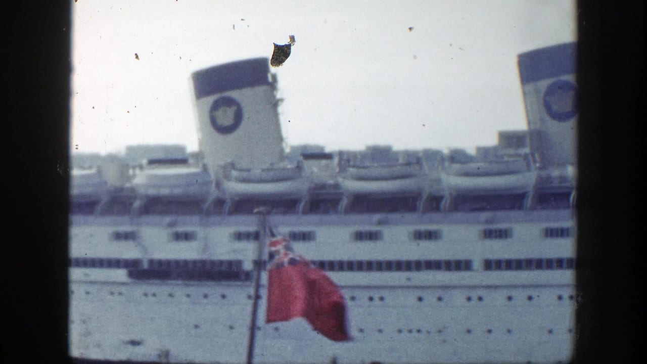 White ocean liner behind a red ensign flag on harbor water.