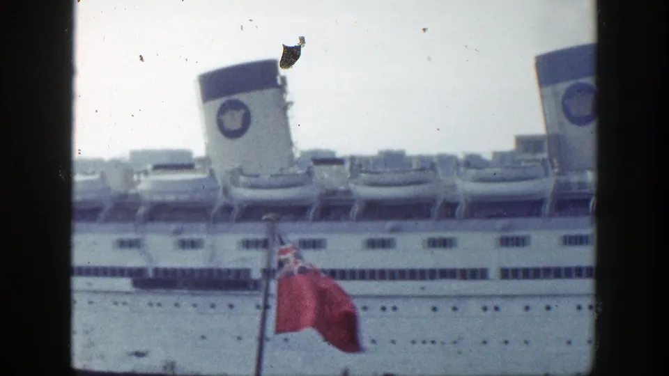 1948 New York harbor view of a white ocean liner with lifeboats and a red ensign flag in the foreground.