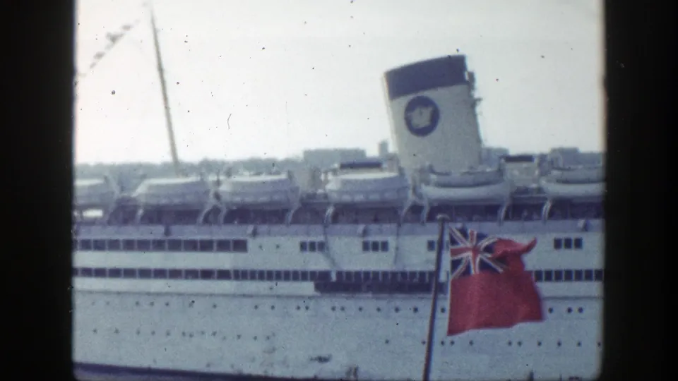 1948 New York home-movie frame showing a white passenger ship, lifeboats, funnel marking, and foreground red ensign.