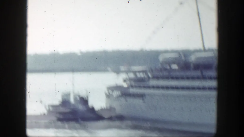 A soft 8mm frame shows a tugboat near the large liner, with the harbor and lifeboats blurred by motion and focus.