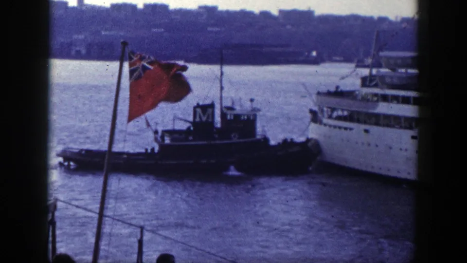 1948 New York harbor frame showing a tugboat alongside a larger vessel, partly framed by a red ensign flag and dark film edges.
