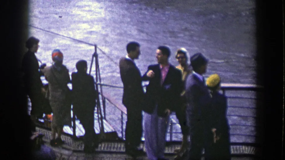 1948 New York shipboard view of passengers conversing or standing on deck, framed by railings and reflective harbor water.