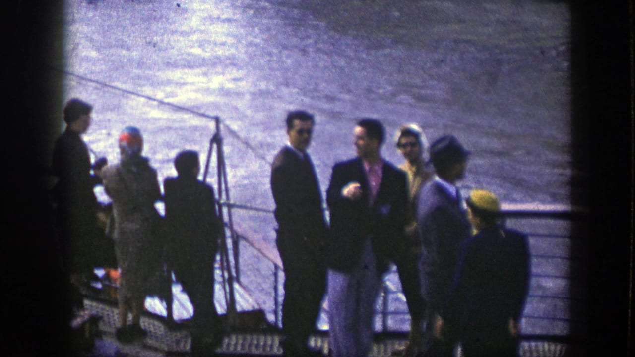 Passengers stand near a ship railing with water behind them.