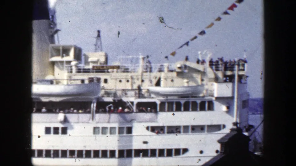 1948 New York home-movie frame of a large white passenger ship with deck passengers, viewed through a dark foreground window frame.