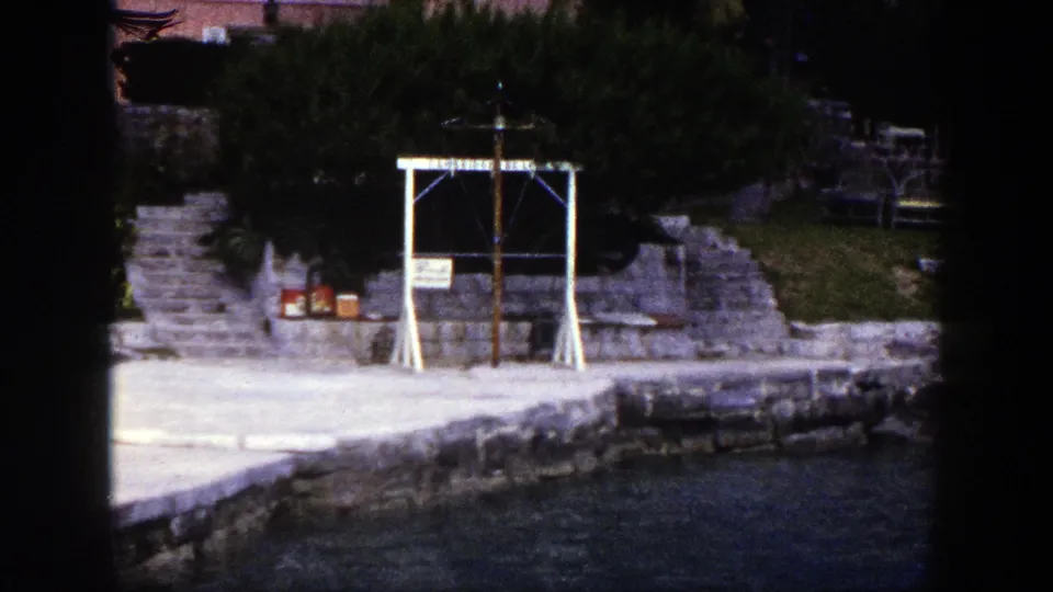 1948 New York home-movie view of a stone shoreline, steps, greenery, and a white wooden religious-looking frame by the water.