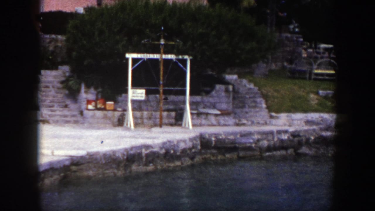 White cross-like waterfront structure beside stone steps and shrubs.
