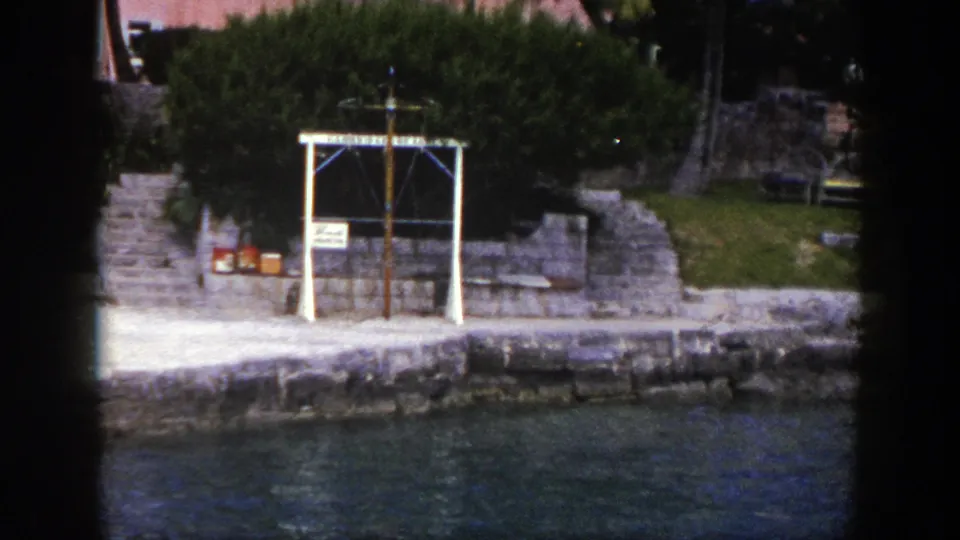 Late-frame view of the New York shoreline feature, showing the white cross-like structure, stone quay, steps, lawn, and water.
