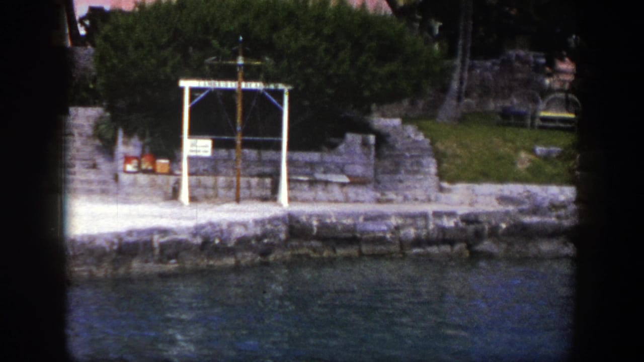 1948 New York 8mm frame showing a stone waterfront, green trees, benches, rippling water, and a white-framed dockside feature.