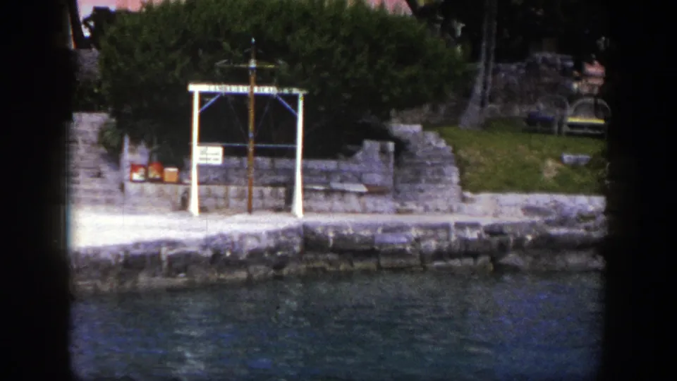 1948 New York 8mm frame showing a stone waterfront, green trees, benches, rippling water, and a white-framed dockside feature.