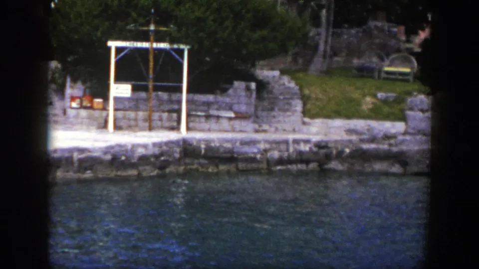 1948 New York boat view of a stone embankment beside water, with trees, benches, steps, and a white dockside frame.