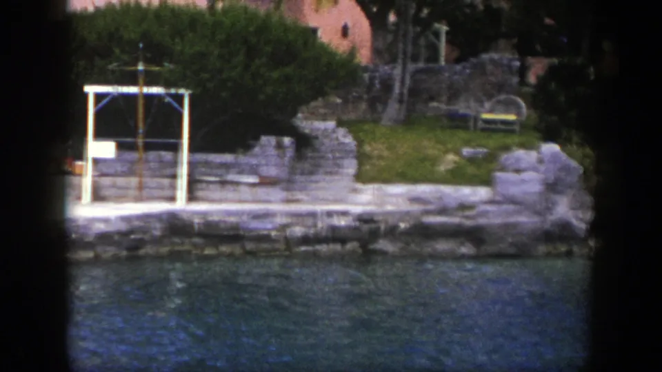 Late frame from 1948 New York 8mm footage showing water, a stone embankment, trees, benches, and a white shoreline frame.