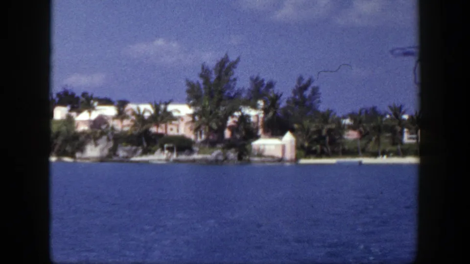 Soft 8mm frame of a palm-lined coastal property and pale buildings across blue water, from the 1948 New York-labeled clip.