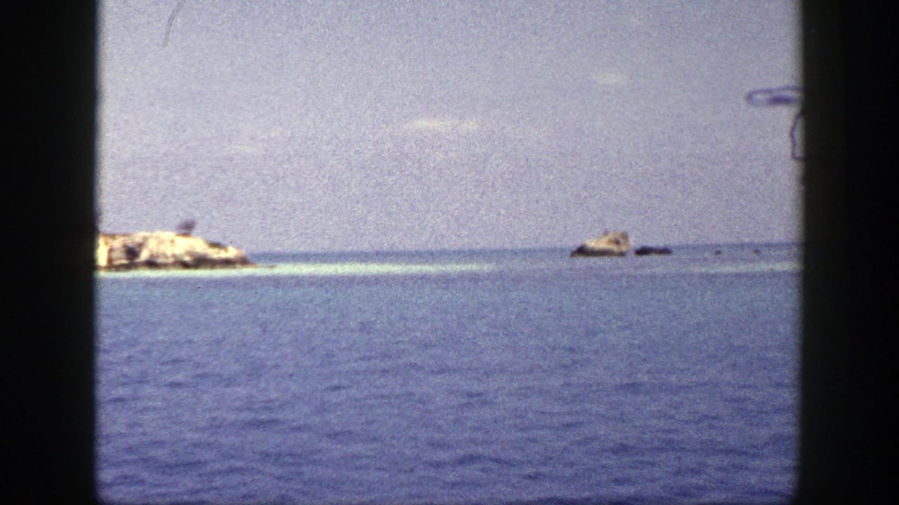 1948 New York 8mm frame showing blue water, pale sky, and tan rock formations viewed from a moving vessel.