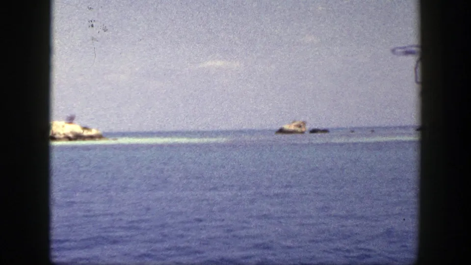 1948 New York coastal view with calm blue ocean, low horizon, and small tan rocks in the distance.