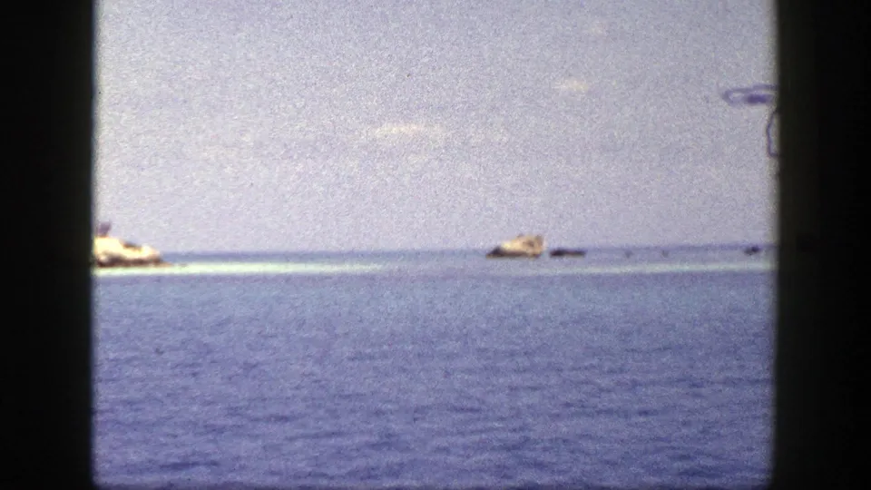 1948 New York 8mm home-movie frame of blue water, faint horizon, and distant tan rocks from a moving vessel.
