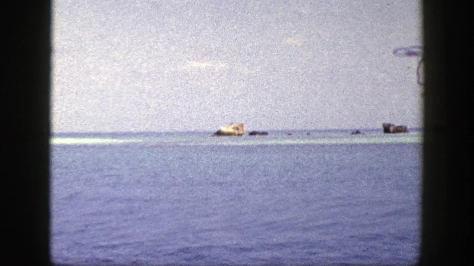 1948 New York 8mm frame with a small tan distant object on calm blue water and several darker shapes along the horizon.