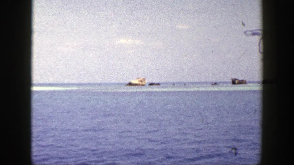 1948 New York 8mm frame showing a wide blue-water view with a tan distant object and dark forms near the horizon.