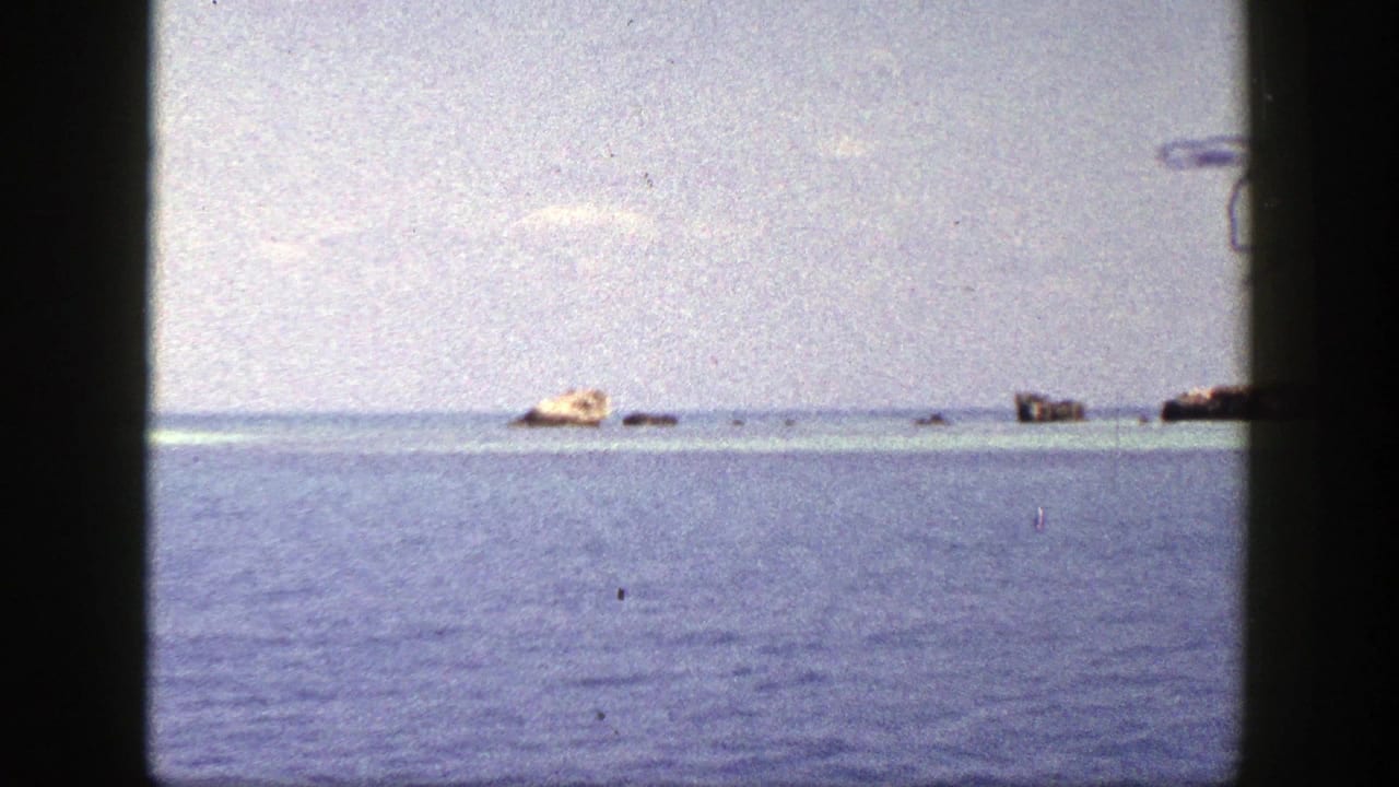 1948 8mm home-movie frame labeled New York, showing open water, distant rocks, and a pale low island through a dark gate edge.