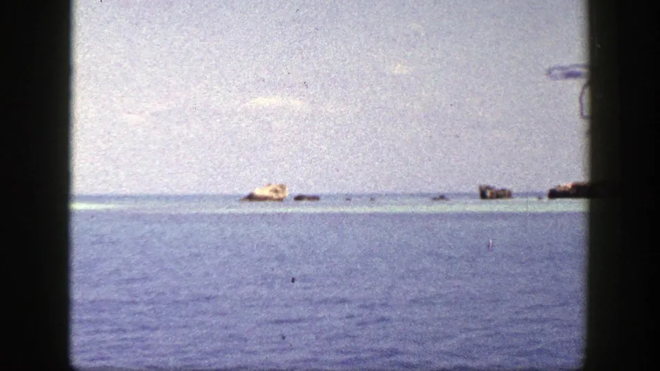 1948 8mm home-movie frame labeled New York, showing open water, distant rocks, and a pale low island through a dark gate edge.