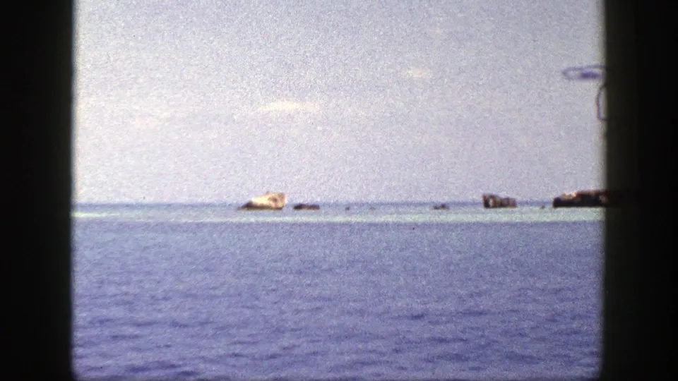 Boat-view 8mm frame with blue water, low horizon, pale landform, and dark film-edge framing from the 1948 New York-labeled clip.
