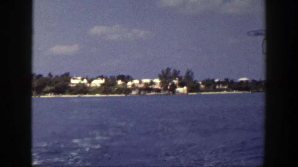Final 1948 8mm frame labeled New York, showing a shoreline with white buildings, dark trees, and calm water from a moving boat.
