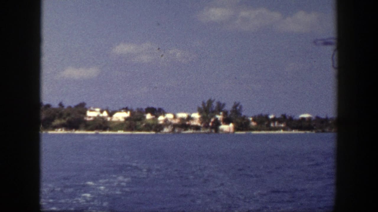 Distant shoreline with white buildings across blue water under scattered clouds.
