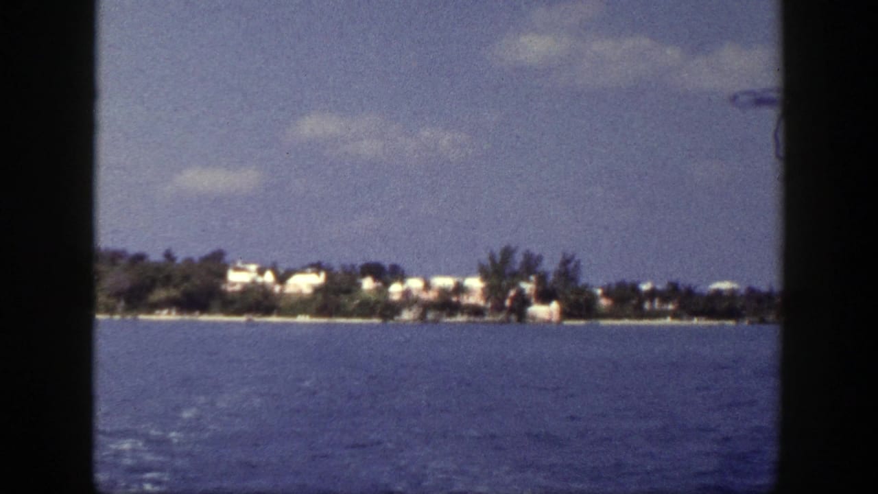 Distant shoreline with white buildings across blue water under a partly cloudy sky.