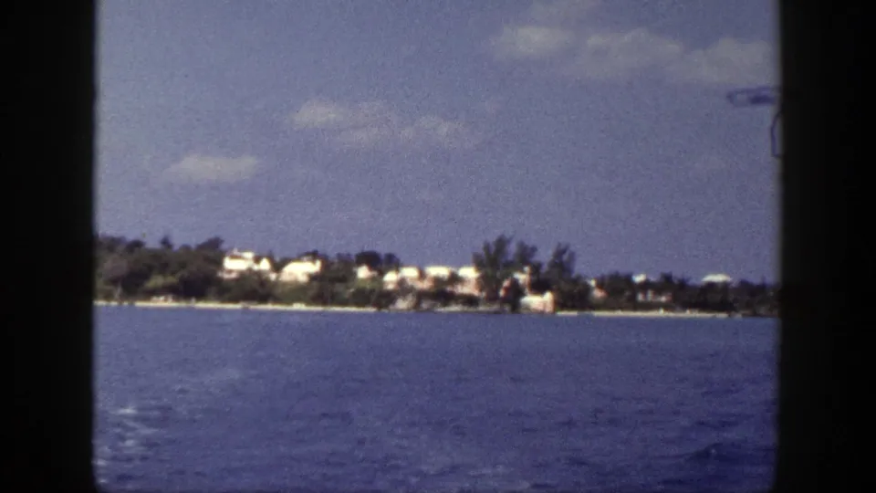 1948 New York shoreline seen from water, with small white buildings among trees and dark frame edges from the vessel view.
