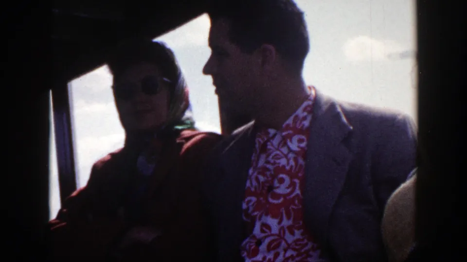 In 1948 New York home-movie footage, a woman in sunglasses and a headscarf sits beside a suited man inside a bus.