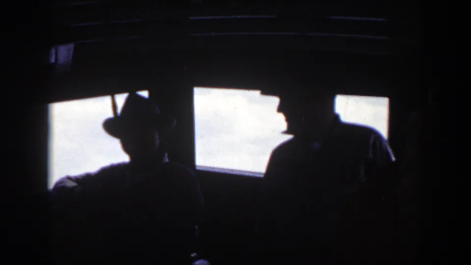 Two adults appear in silhouette inside the boat cockpit, including one in a brimmed hat, with bright New York daylight behind them.