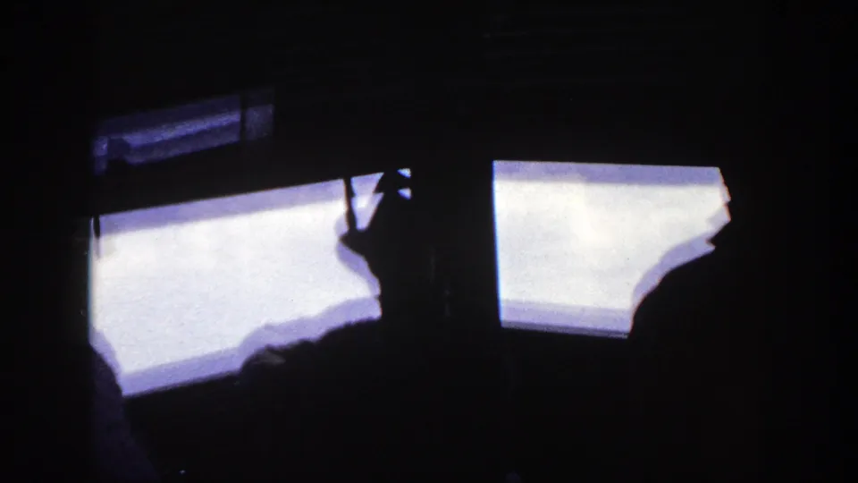 Silhouetted figures aboard a ship appear to look through large windows in this 1948 New York-labeled home-movie frame.