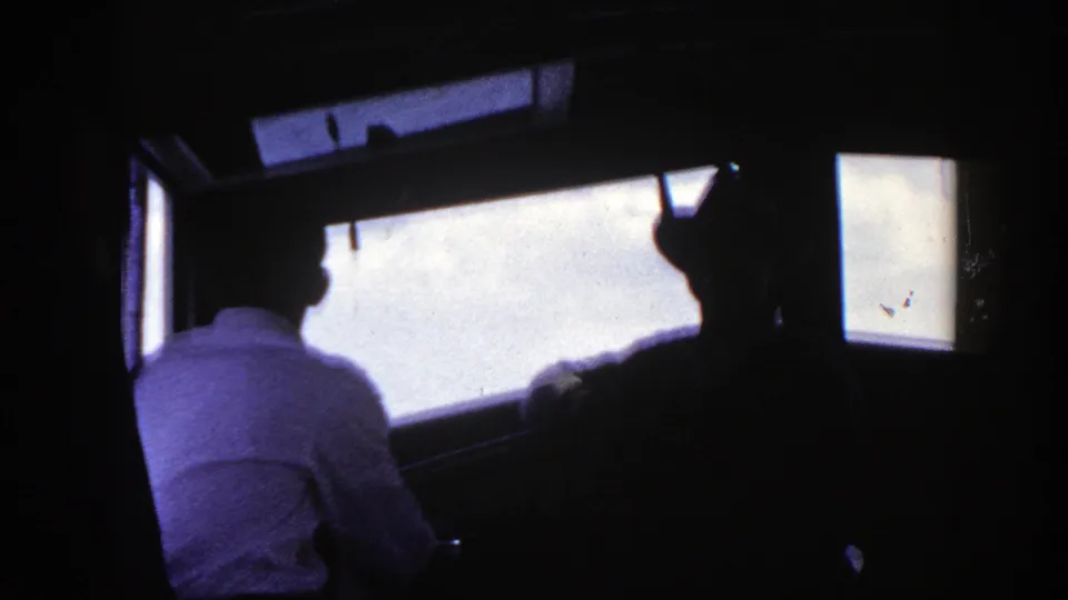 Shipboard interior frame shows a seated man in a light shirt and nearby silhouettes against bright windows, supported as 1948 New York footage.