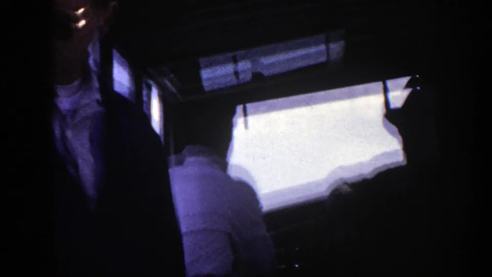 A dim 1948 New York travel frame with a partly visible adult man and seated passengers near bright windows.