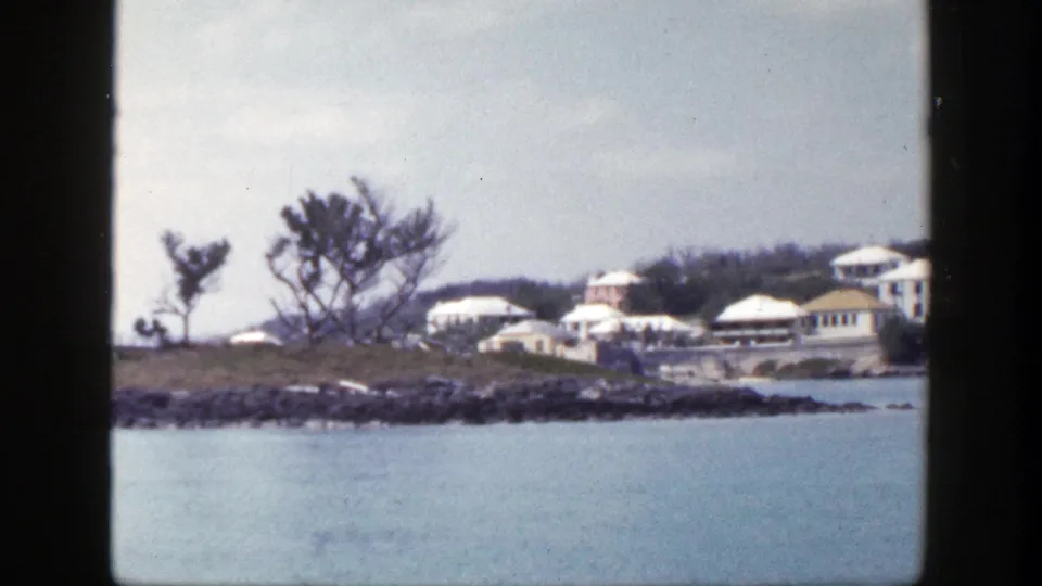 1948 New York 8mm frame with blue water in the foreground and distant coastal buildings along a rocky shoreline.