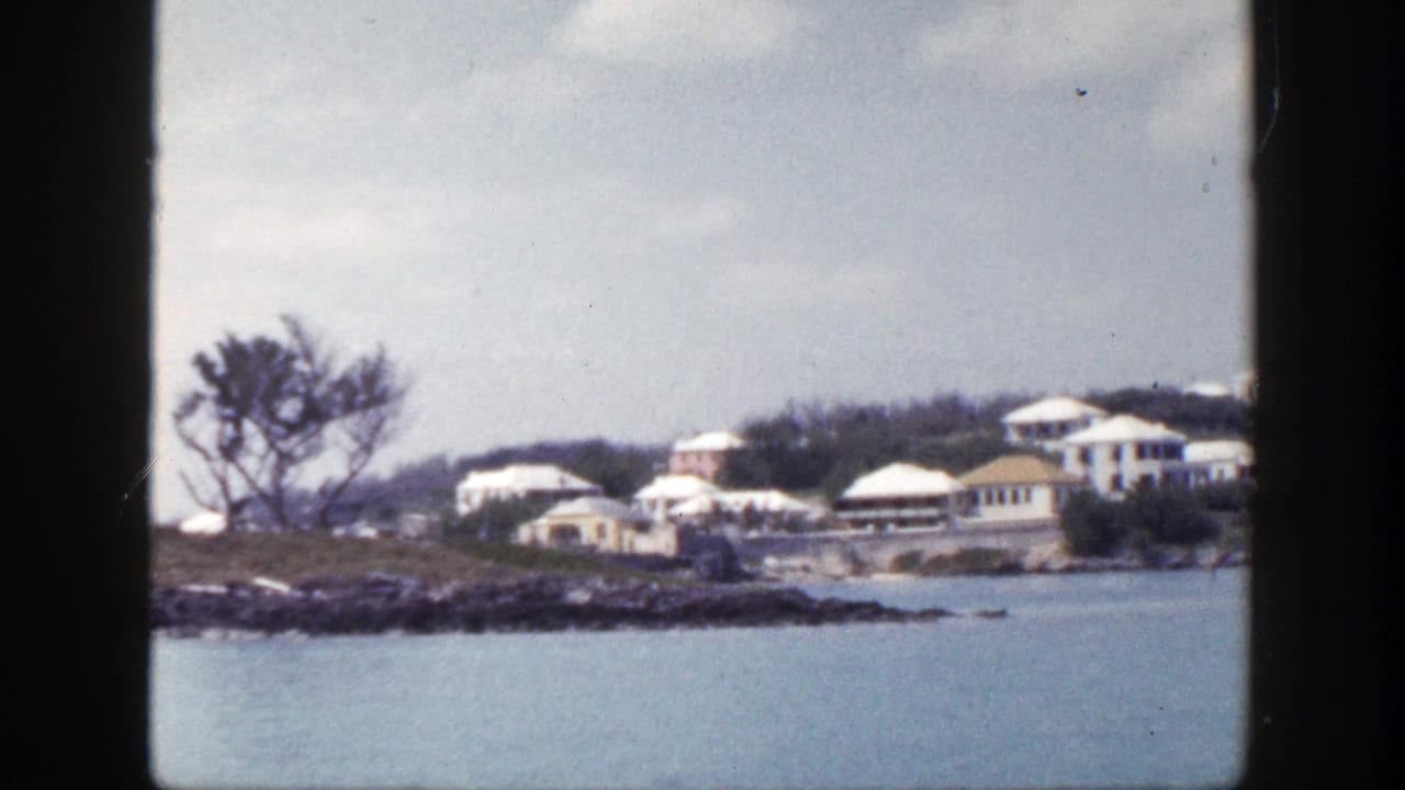Waterfront buildings and trees seen from across blue water, framed by dark film edges.