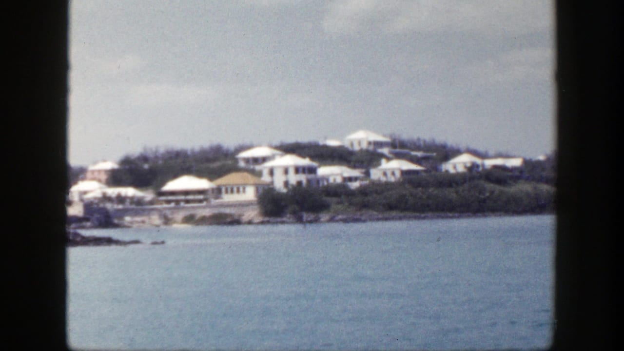 White houses on a green coastal hillside across blue water.