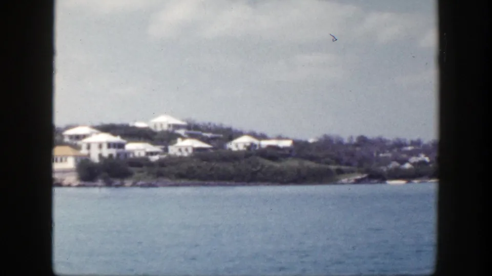Vintage 8mm frame of shoreline houses and trees viewed from the water, consistent with the 1948 New York reel metadata.