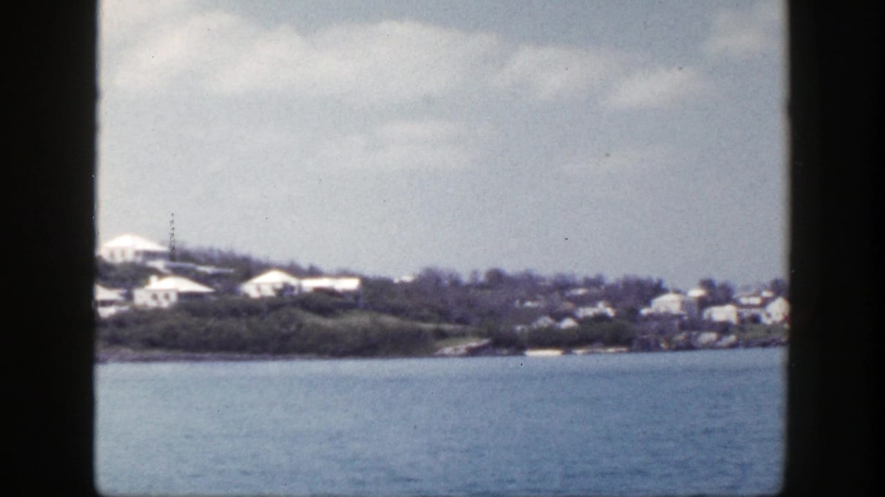 Distant shoreline with pale buildings across blue water under a cloudy sky.