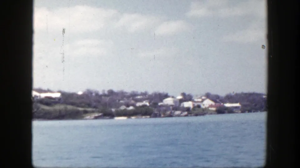 1948 8mm view of a New York coastal settlement with trees, rooftops, and blue water in the foreground.