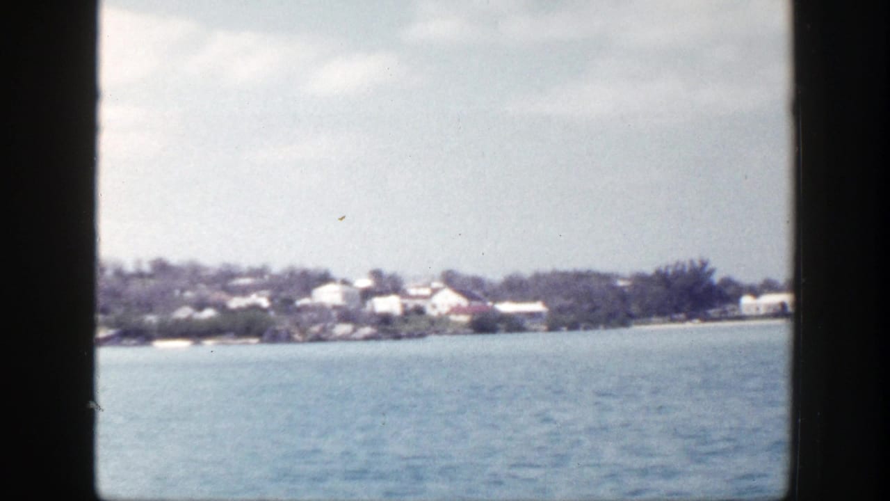 Distant shoreline across blue water with pale buildings and dark film-frame edges.