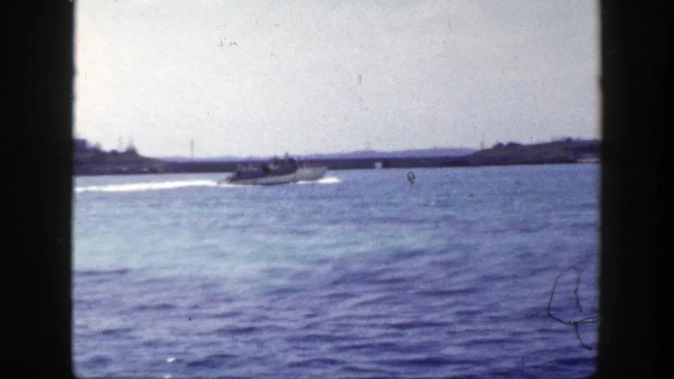 1948 New York home-movie frame showing a distant motorboat on rippled blue water, backed by a low shoreline and pale sky.