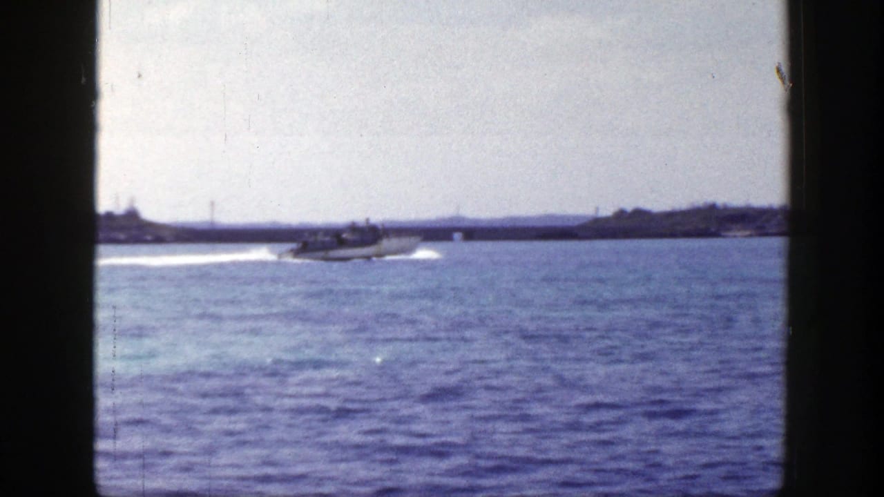 Small motorboat crossing calm blue water with a distant shoreline behind it.