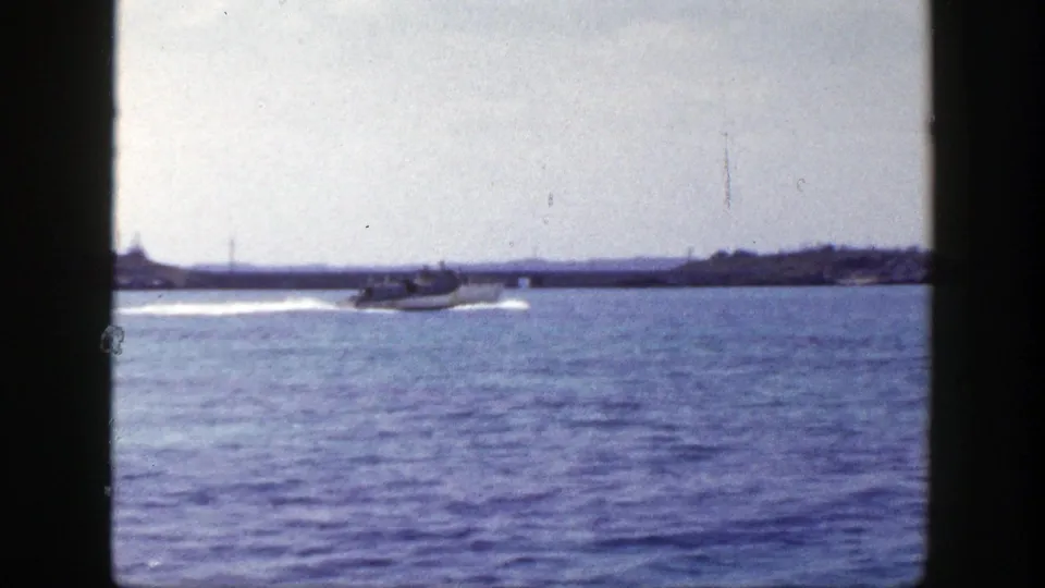 1948 New York coastal home-movie frame with a small motorboat passing over calm blue water under cloudy sky.