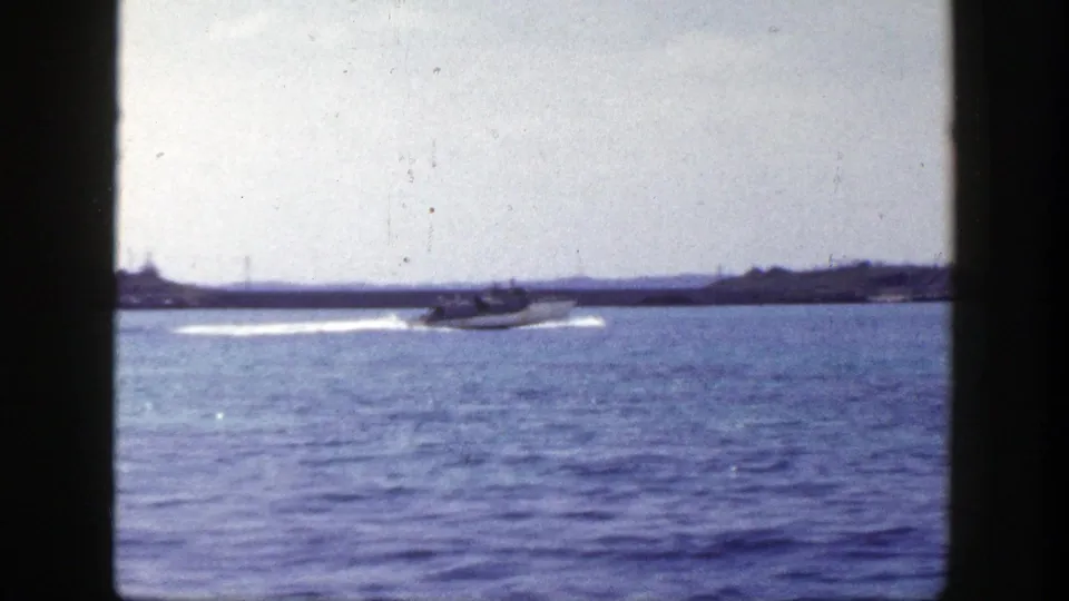 1948 New York coastal frame showing a small motorboat and wake against a low shoreline and cloudy sky.