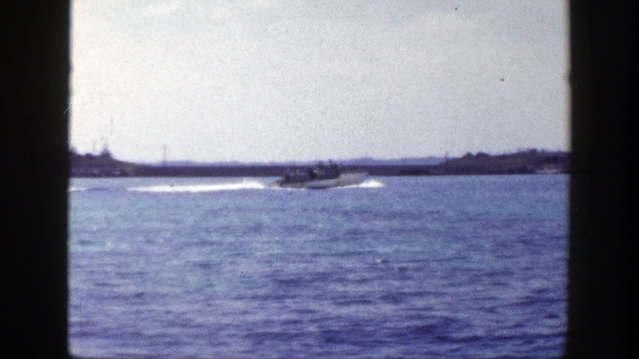 Small motorboat crossing calm water with a distant shoreline behind it.