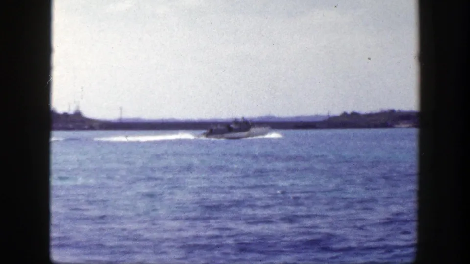 1948 New York 8mm frame showing a small motorboat moving across open water with a low shoreline in the distance.