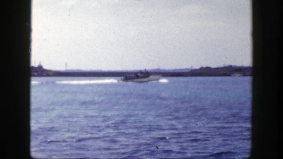 1948 New York home-movie frame with a motorboat crossing blue water and a low shoreline visible beyond it.